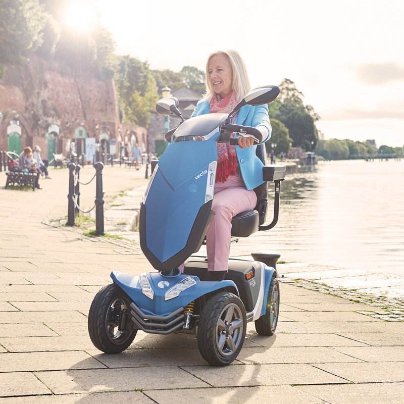 Scooter Vecta Sport Mujer conduciendo scooter Vecta Sport azul junto a un paseo marítimo