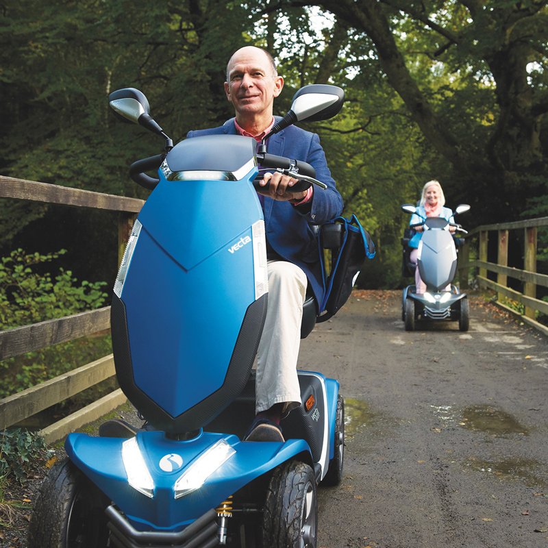 Scooter Vecta Sport Hombre conduciendo scooter Vecta Sport azul por camino forestal