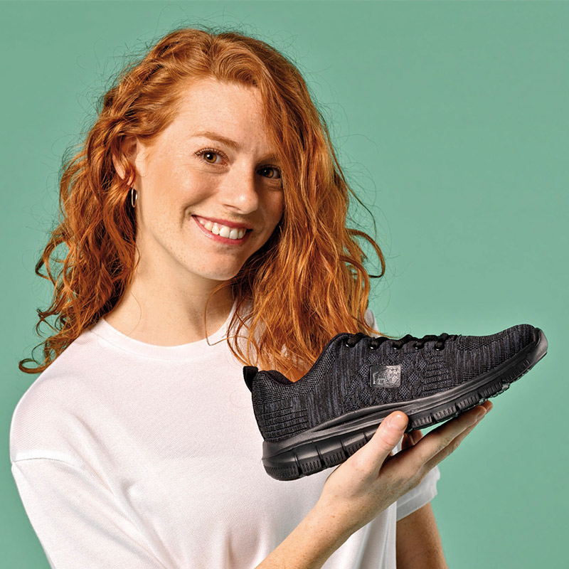 Zapatillas casual unisex 21014 Mujer pelirroja sonriente con zapatilla unisex negra en la mano