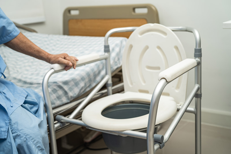 Cómo ayudar a una persona mayor a ir al baño de forma segura Persona mayor utilizando una silla con orinal colocada al lado de la cama