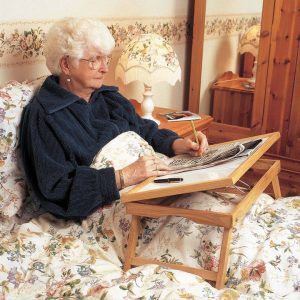 Mujer mayor usando la mesita para cama NANI ajustable para escribir desde la cama