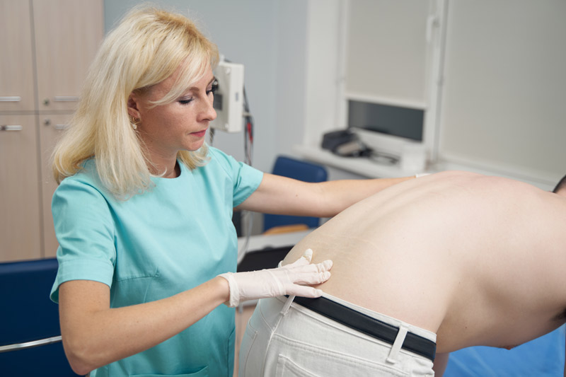Dolor en el coxis Profesional de la salud palpando la parte baja de la columna en un paciente inclinado con dolor de coxis