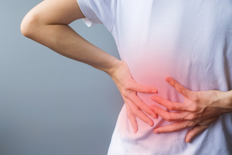 Mujer con dolor en la parte baja de la espalda, con la mano sobre la zona lumbar