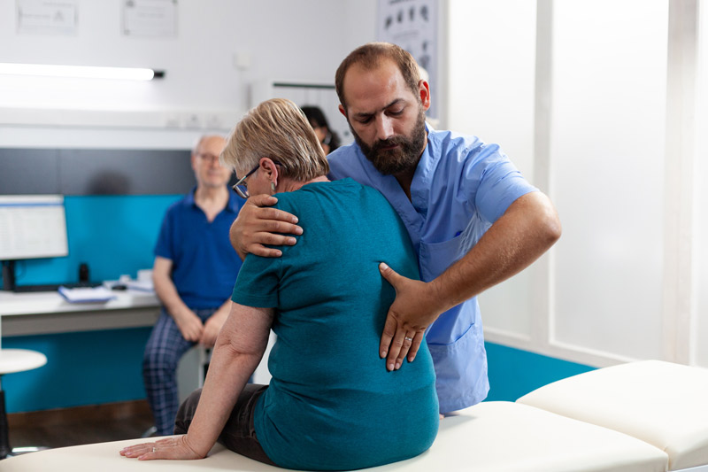 Dolor en las lumbares: causas, síntomas y alivio seguro Profesional sanitario palpando la zona lumbar de una paciente sentada