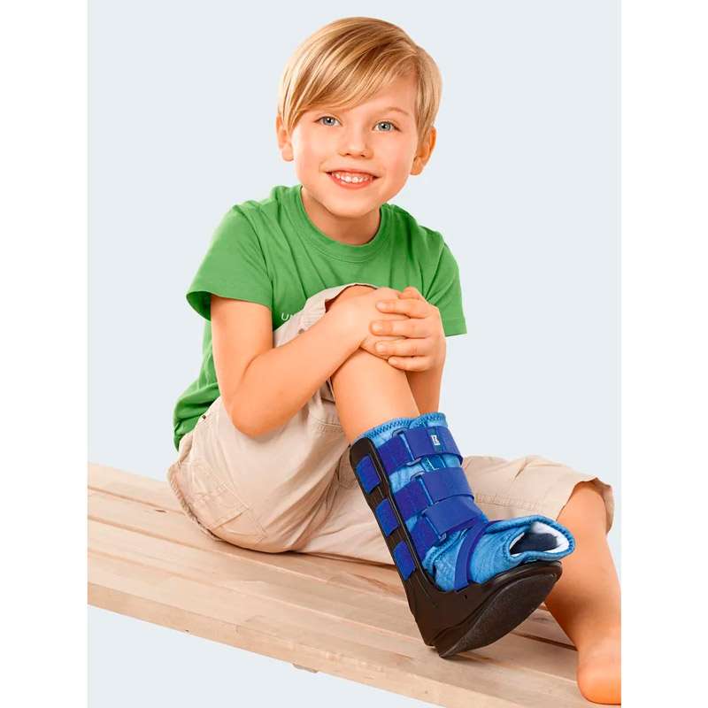 Walker infantil Boot Kidz Niño sentado con walker infantil Boot Kidz azul colocado en la parte inferior de la pierna y el pie